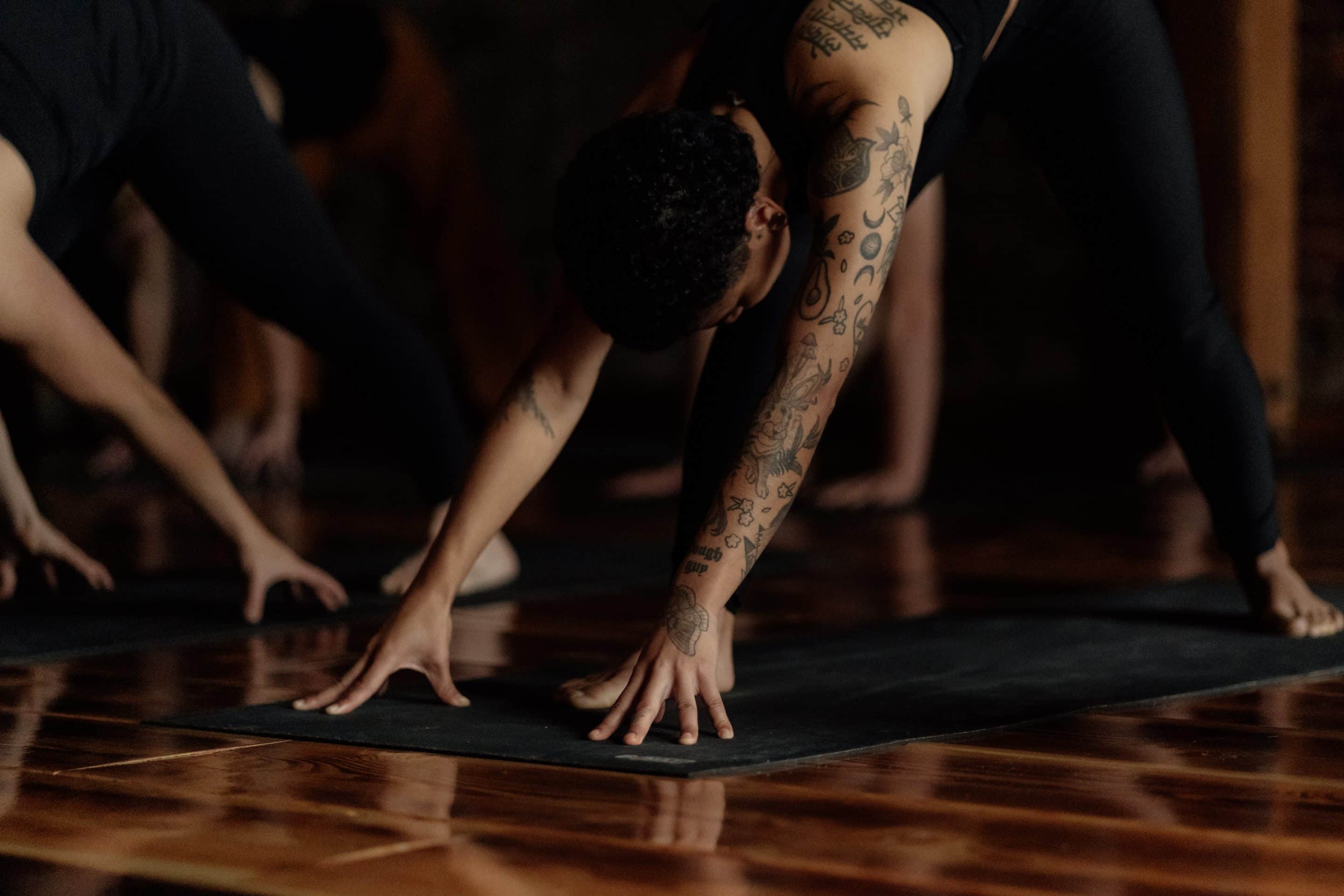 14 Tips to Find the Perfect Yoga Teacher Training Program A woman with tattoos doing the Downward Dog pose during yoga practice.