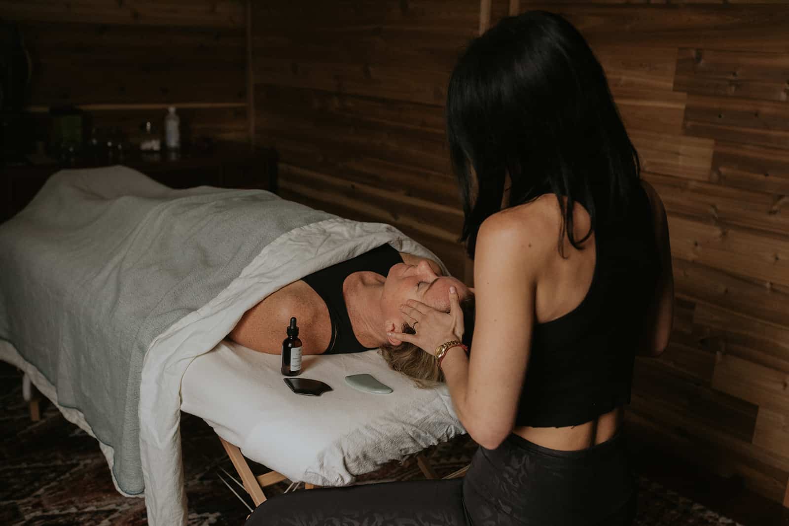 A woman gently cradles another's head in her hands, preparing to begin a therapeutic session aimed at relaxation and healing in her acupuncture session.